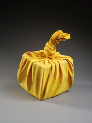Sculpture jaune en forme de furoshiki noué noué autour d'un cube